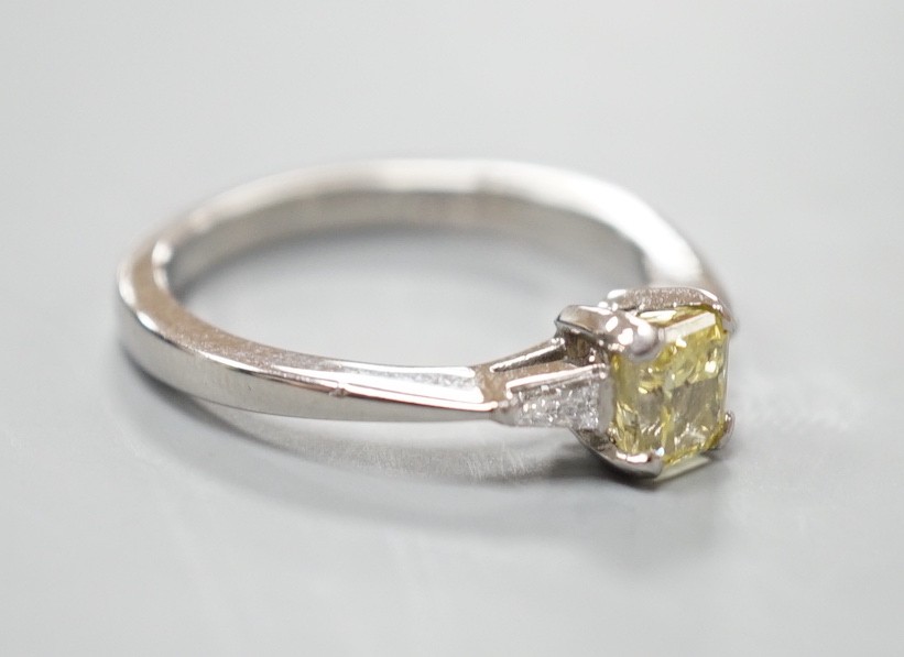 A modern platinum and single stone fancy yellow diamond set ring, with trapeze cut diamond set shoulders, size N, gross weight 4.6 grams